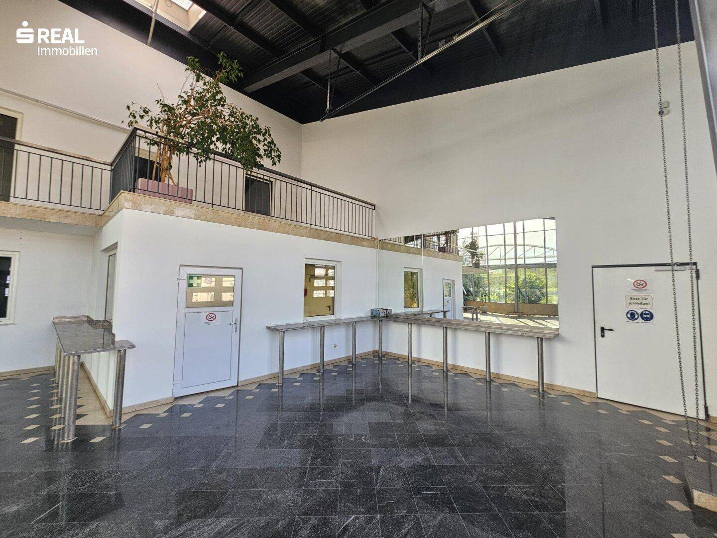 Helle Halle mit dunklem Steinboden, hohen Decken und einem offenen Galeriebereich mit Theken.