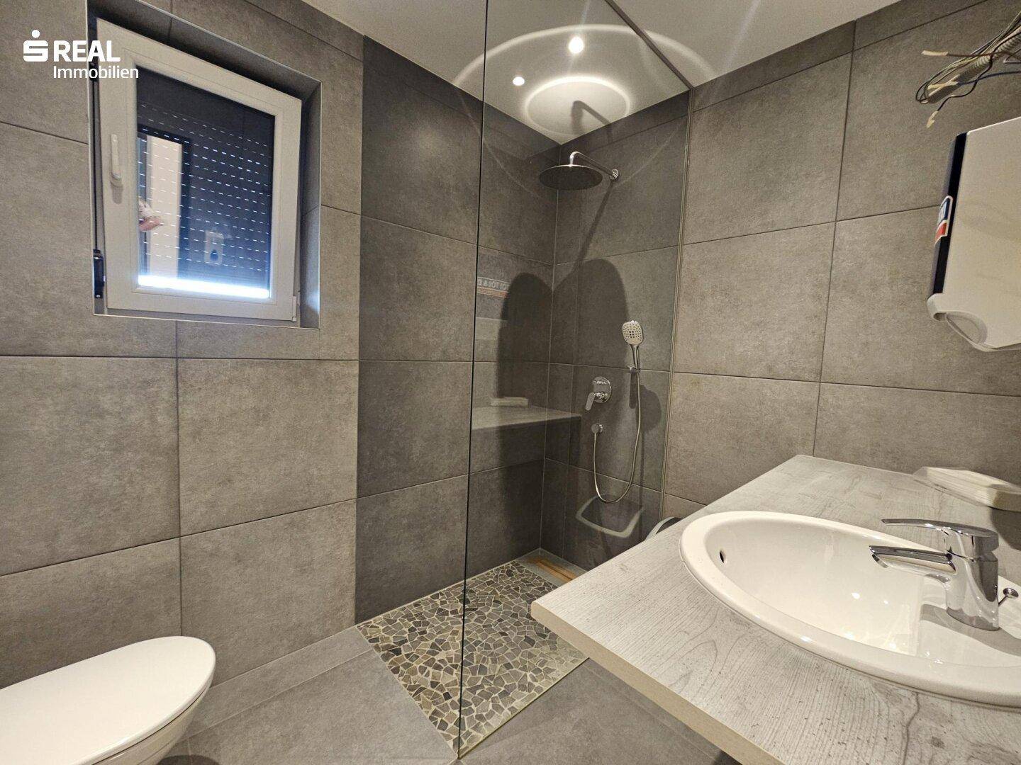 Modernes Badezimmer mit grauen Fliesen, ebenerdiger Dusche und Fenster.