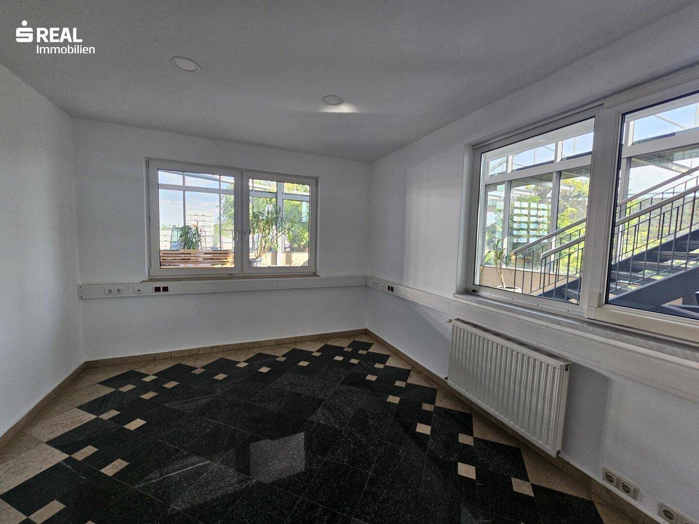 Leeres Büro mit Fenstern, die einen Blick auf die umliegende Struktur und Treppe bieten.
