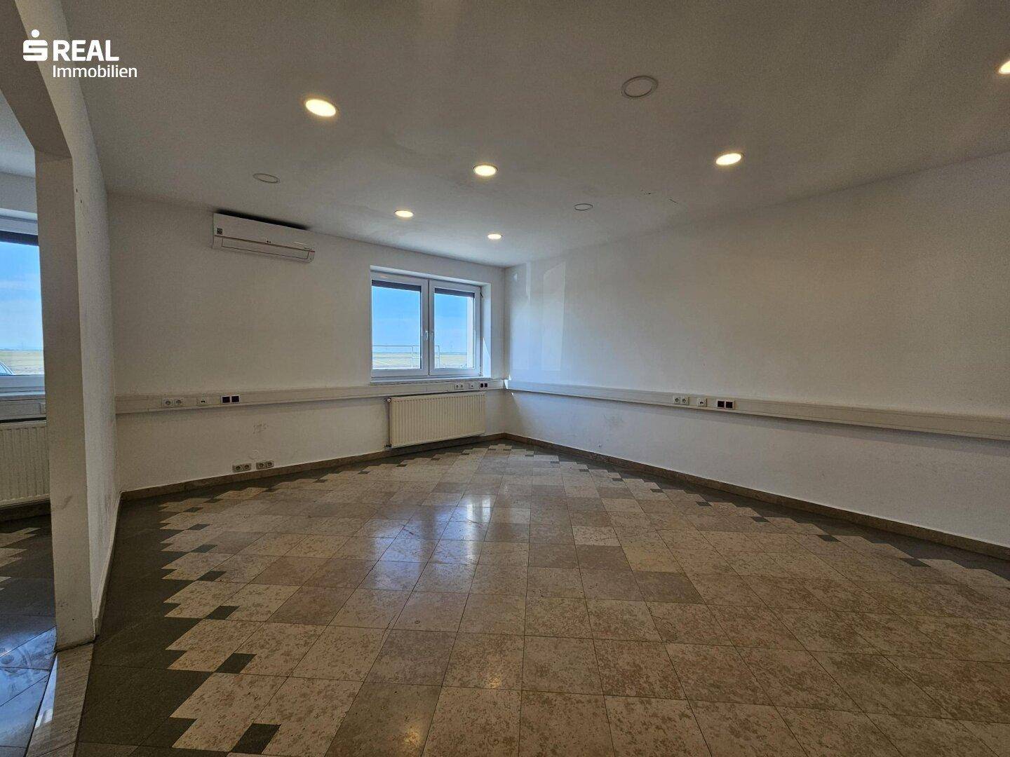 Leeres Büro mit hellen Wänden, Einbaustrahlern und gemustertem Fliesenboden.
