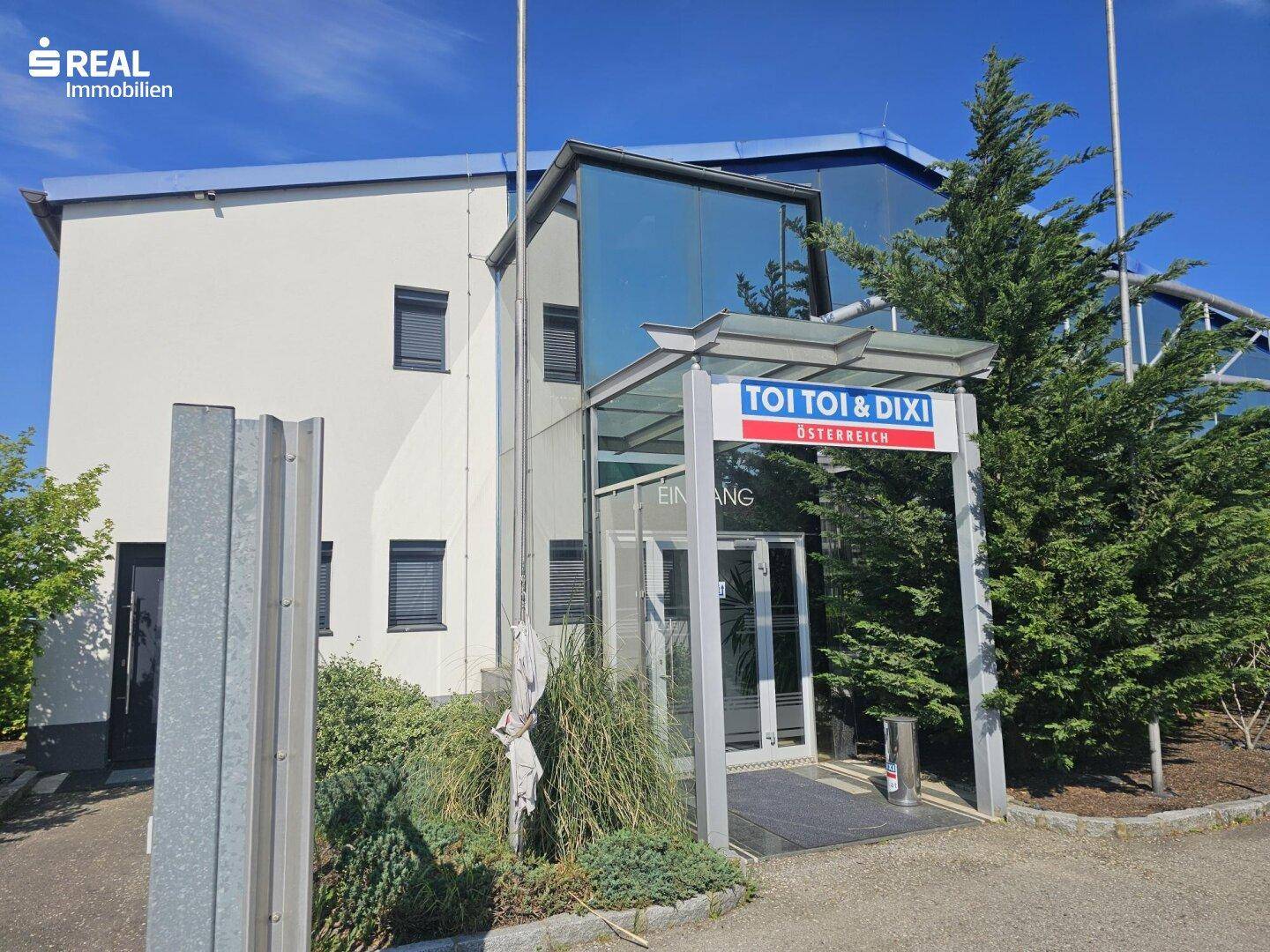 Modernes Geschäftsgebäude mit Glasfassade und Eingangsbereich, umgeben von Grünflächen.