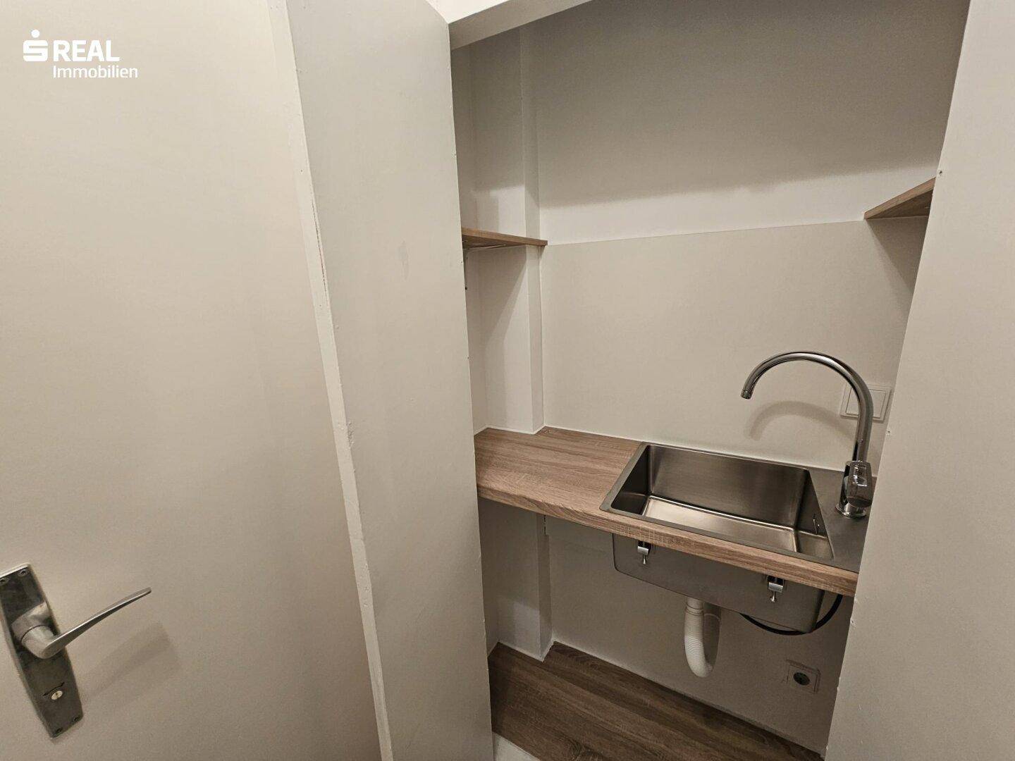 Kleiner Raum mit Spülbecken, Holzablage und Regalen, ideal als Hauswirtschaftsraum.