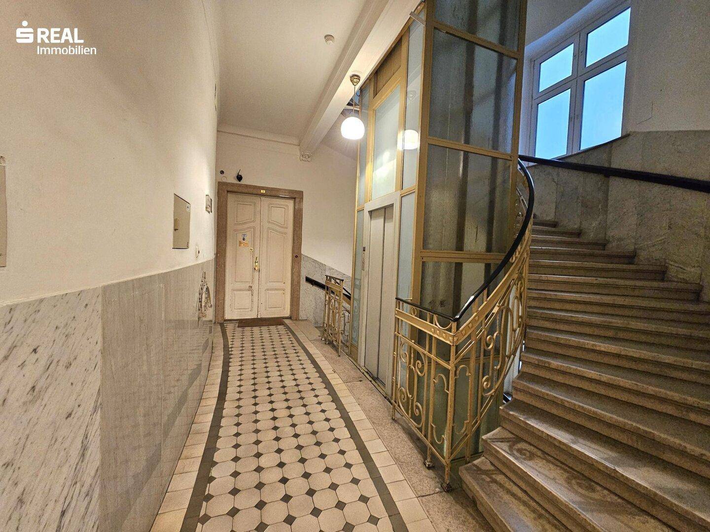 Historisches Treppenhaus mit Marmorverkleidung, kunstvollem Geländer und einem Aufzug.