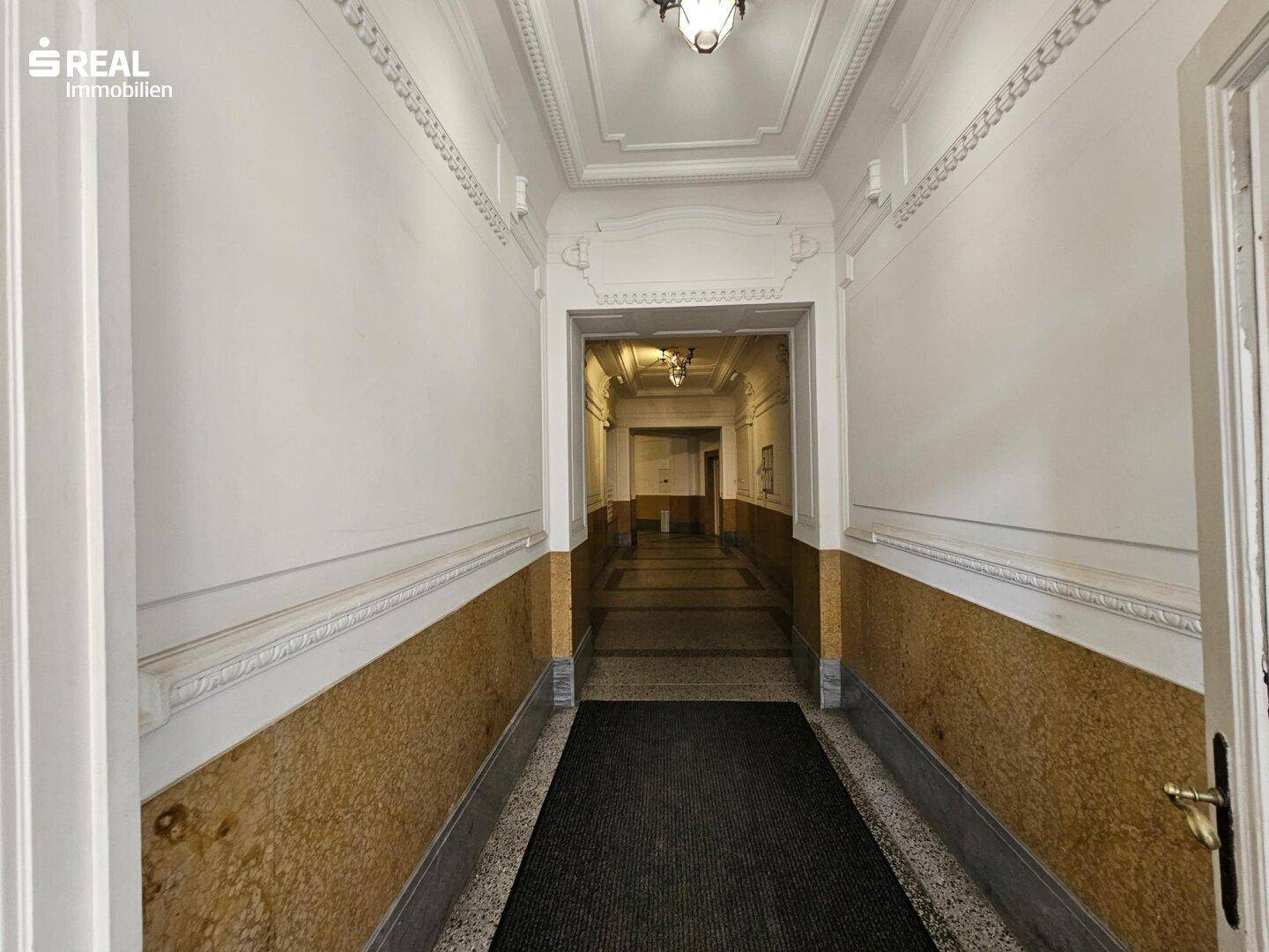 Langer Flur in einem Altbau mit Stuckdecken, Marmorverkleidung und Terrazzoboden.