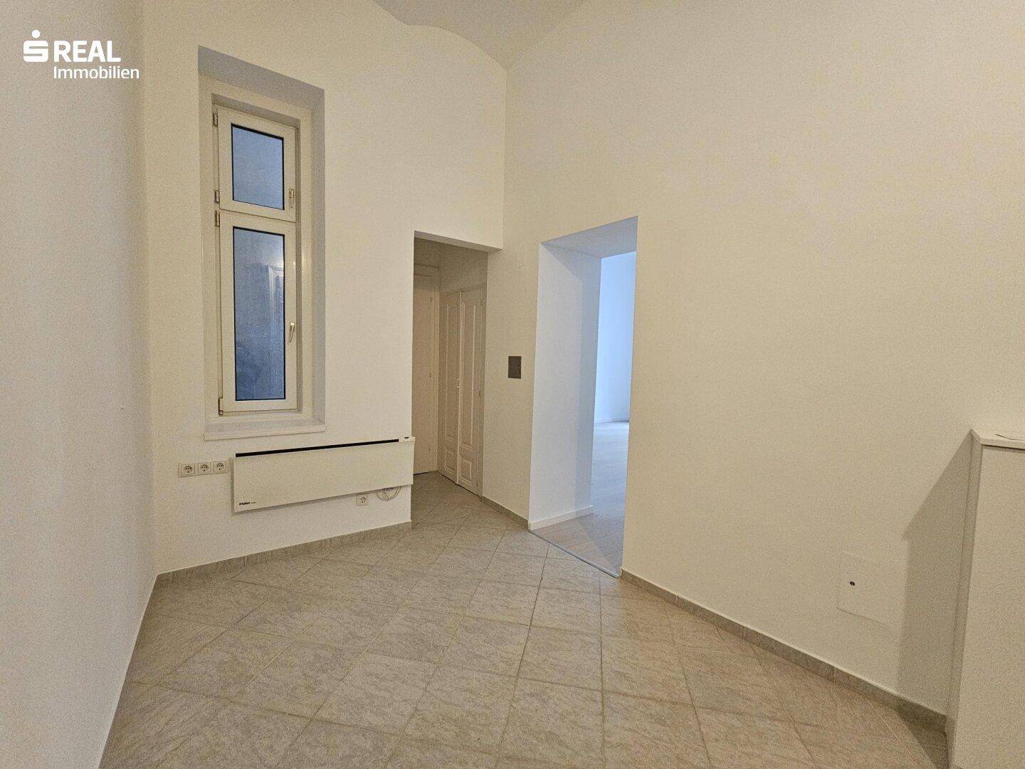 Heller Flur mit Fliesenboden, einem hohen Fenster und Durchgängen zu angrenzenden Räumen.