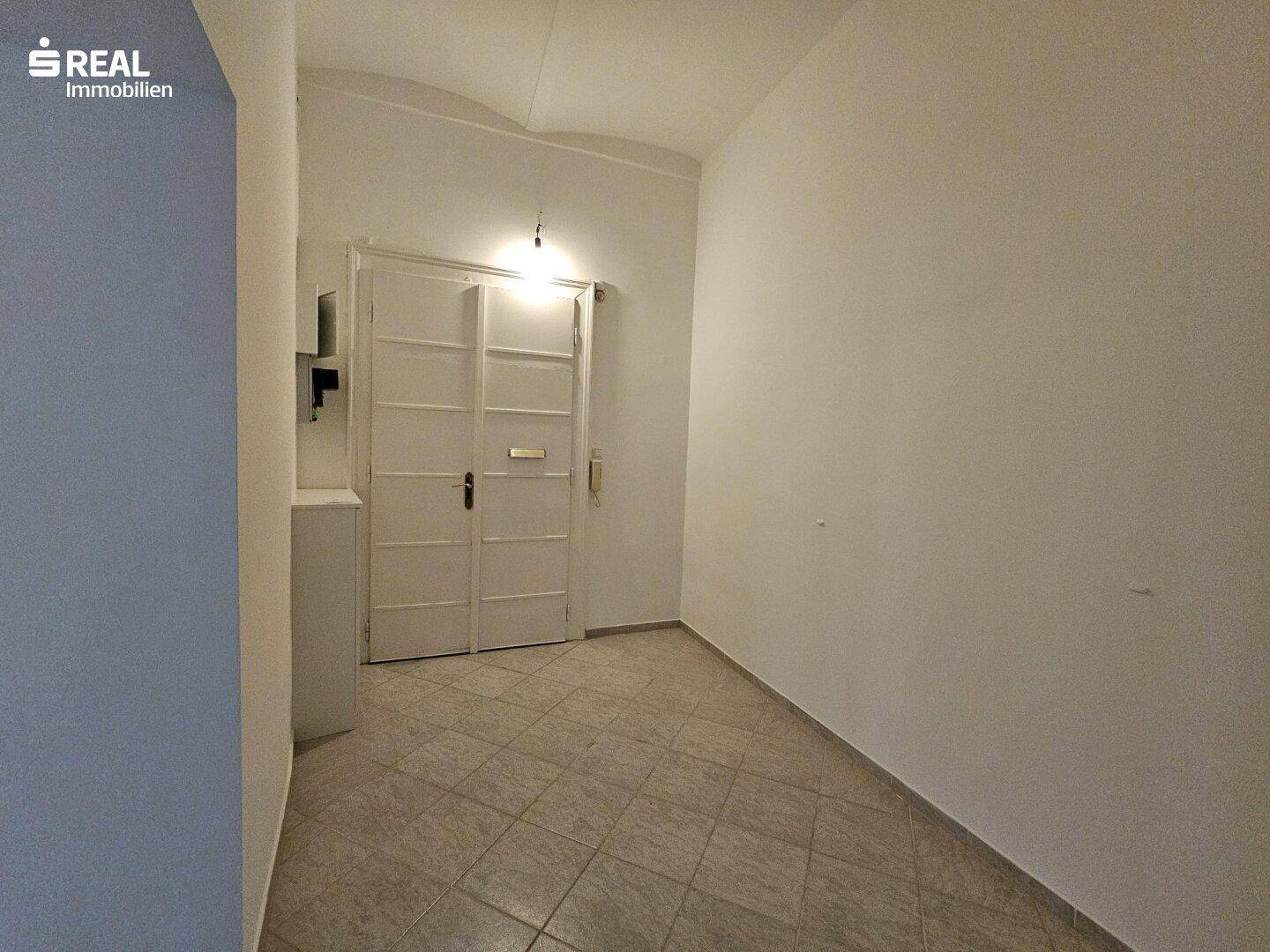 Eingangsbereich mit Fliesenboden und einer weißen Doppeltür, die in die Wohnung führt.