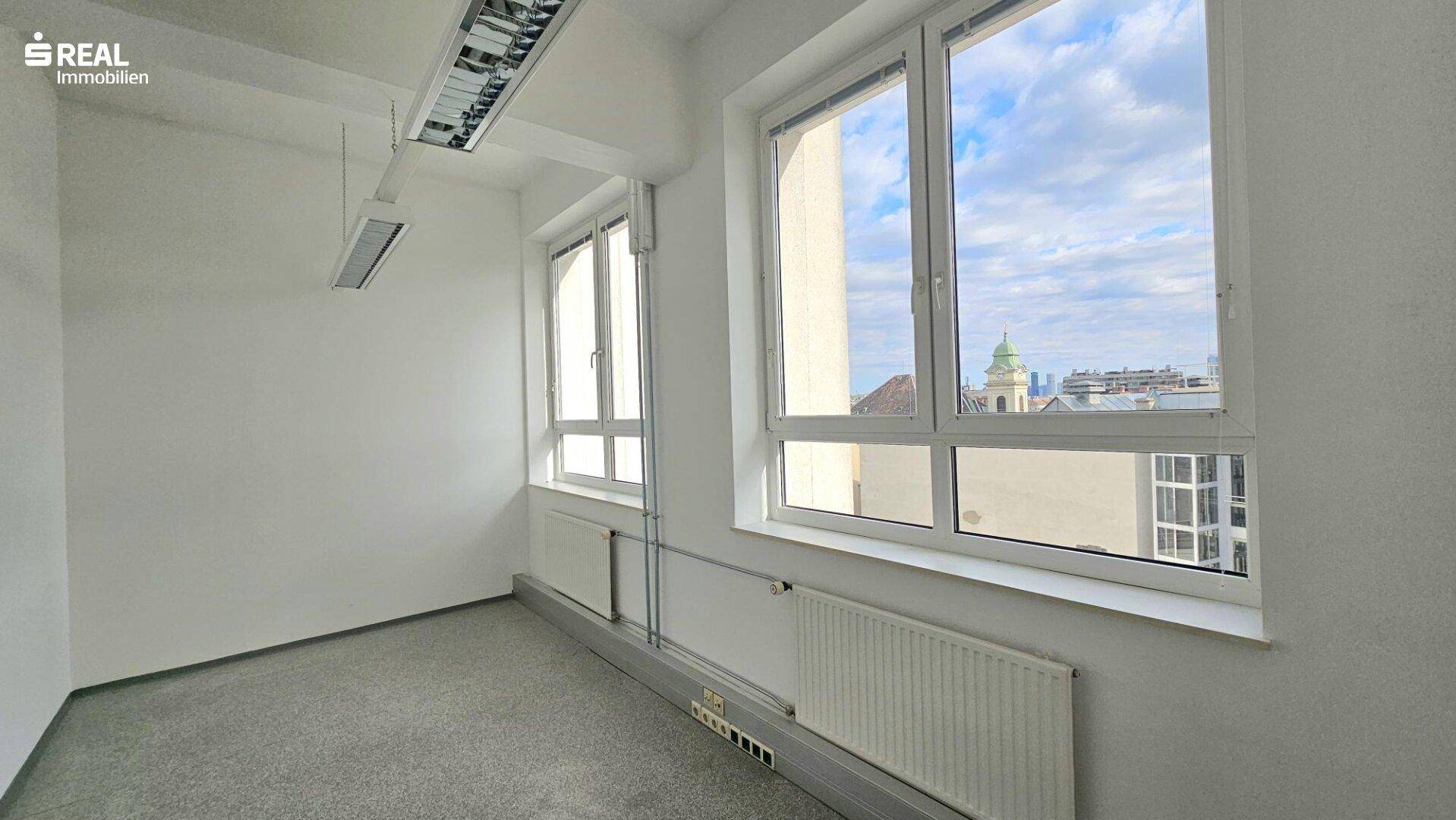 Heller Büroraum mit großen Fenstern, die einen Blick auf die Stadt und den Himmel bieten.