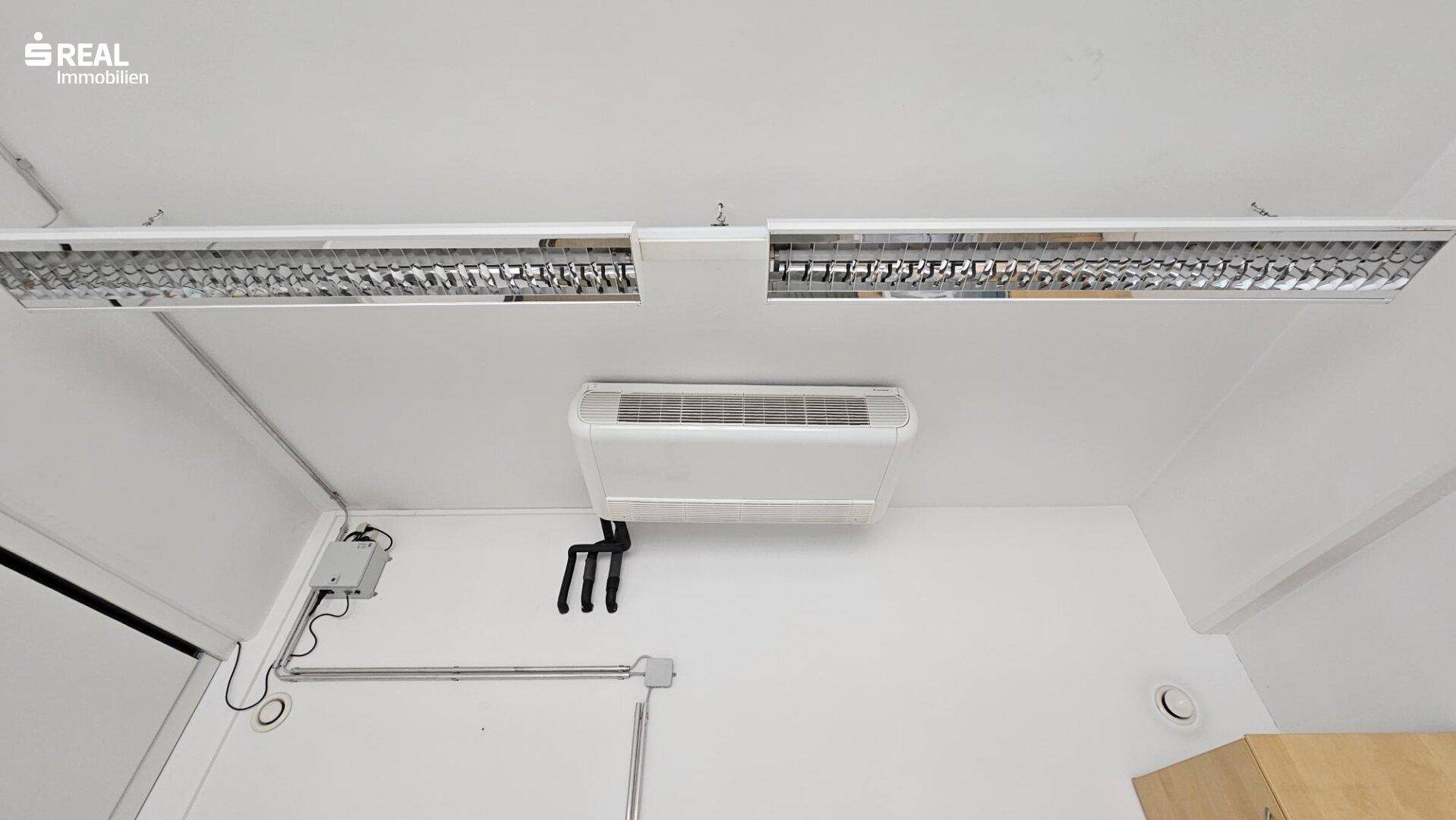 Deckenansicht mit Klimaanlage und Leuchtstoffröhren in einem modernen Büroraum.