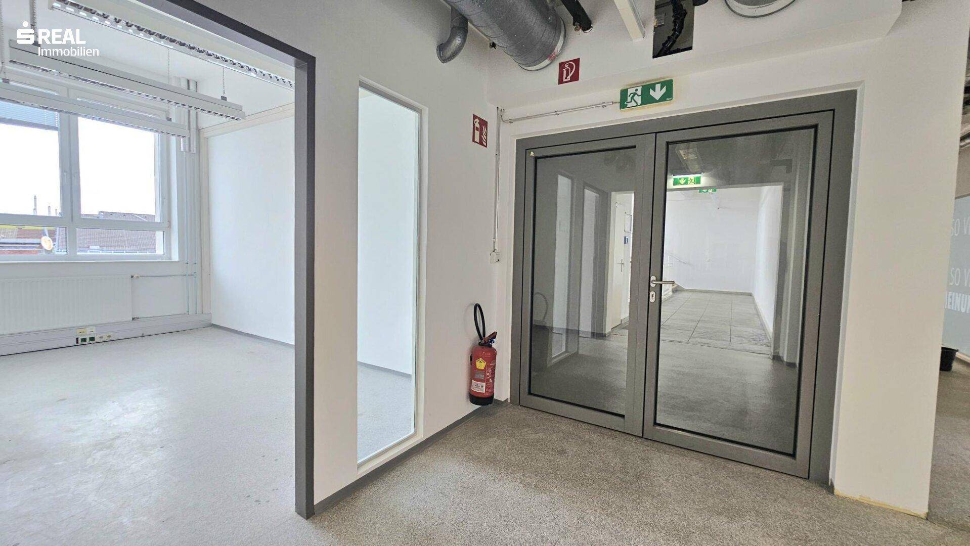 Flur mit Glastüren, Feuerlöscher und Zugang zu weiteren Büroräumen.