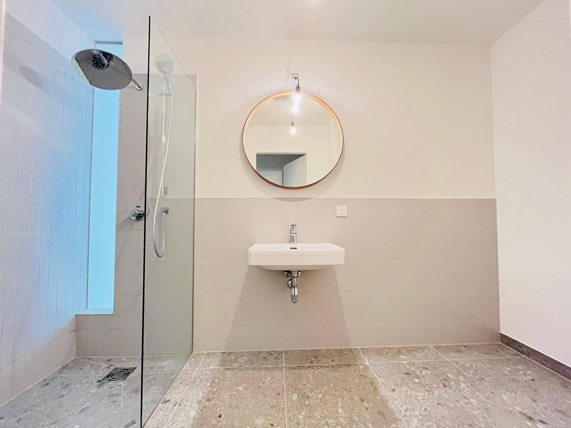 Modernes Badezimmer mit ebenerdiger Dusche, Einzelwaschbecken und rundem Spiegel.