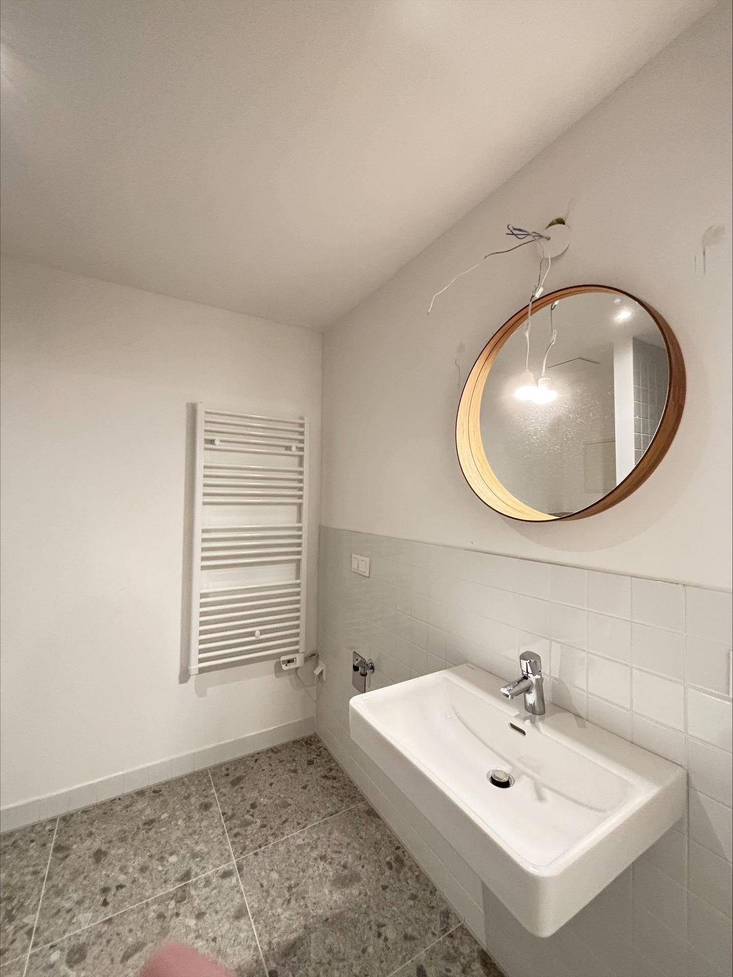 Helles Badezimmer mit modernem Waschbecken, rundem Spiegel und Handtuchheizkörper.