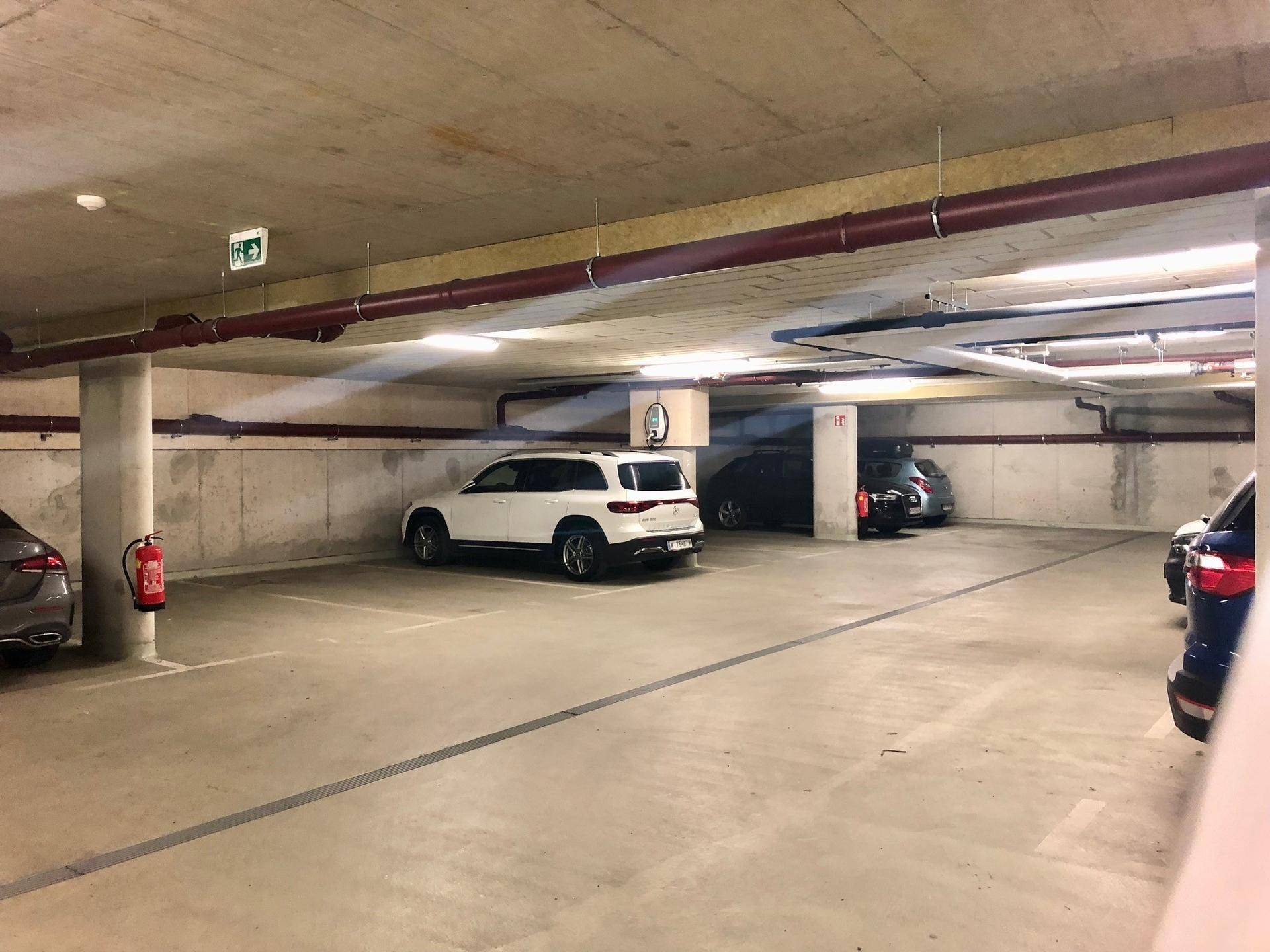 Helle Tiefgarage mit Betonstruktur, mehreren Fahrzeugen und klarer Beleuchtung an der Decke.