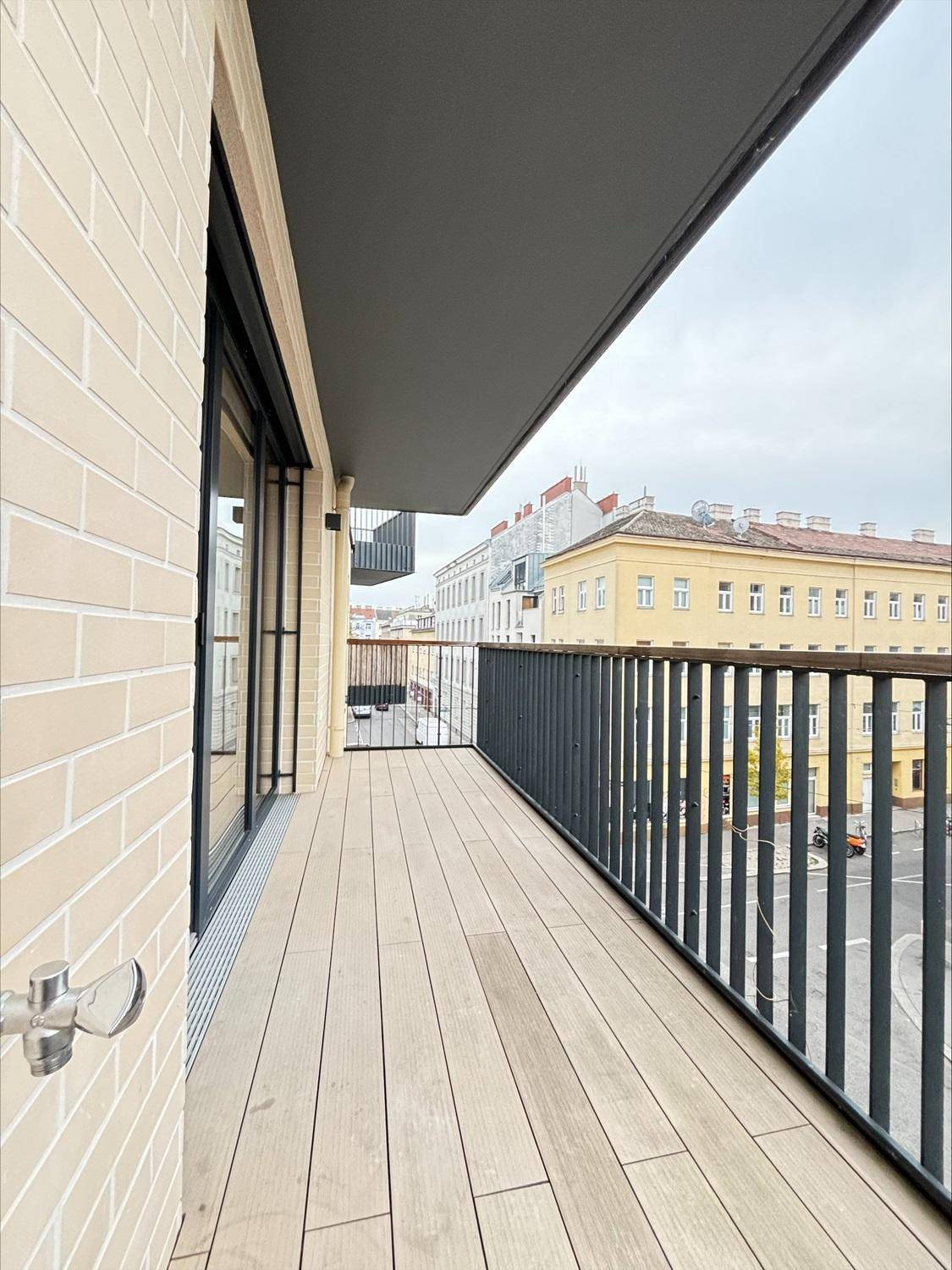 Langer Balkon mit Holzboden und Metallgeländer, bietet Stadtblick.