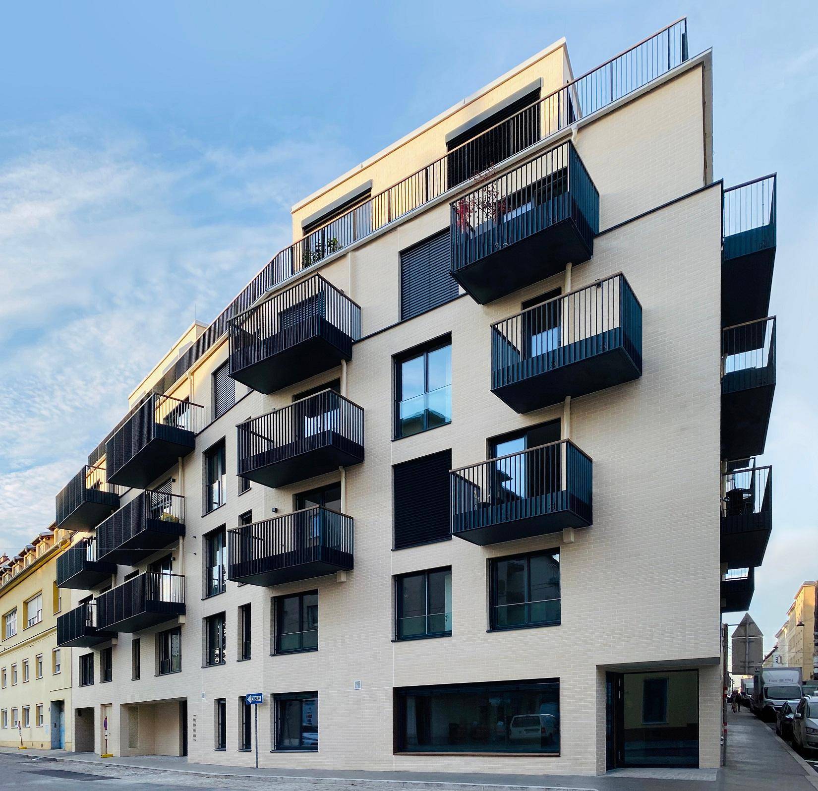 Modernes Mehrfamilienhaus mit vielen Balkonen und großen Fenstern in städtischer Umgebung.