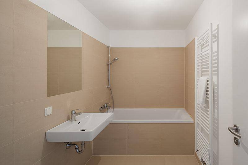 Modernes Badezimmer mit beigefarbenen Fliesen, Badewanne und einem schwebenden Waschbecken.