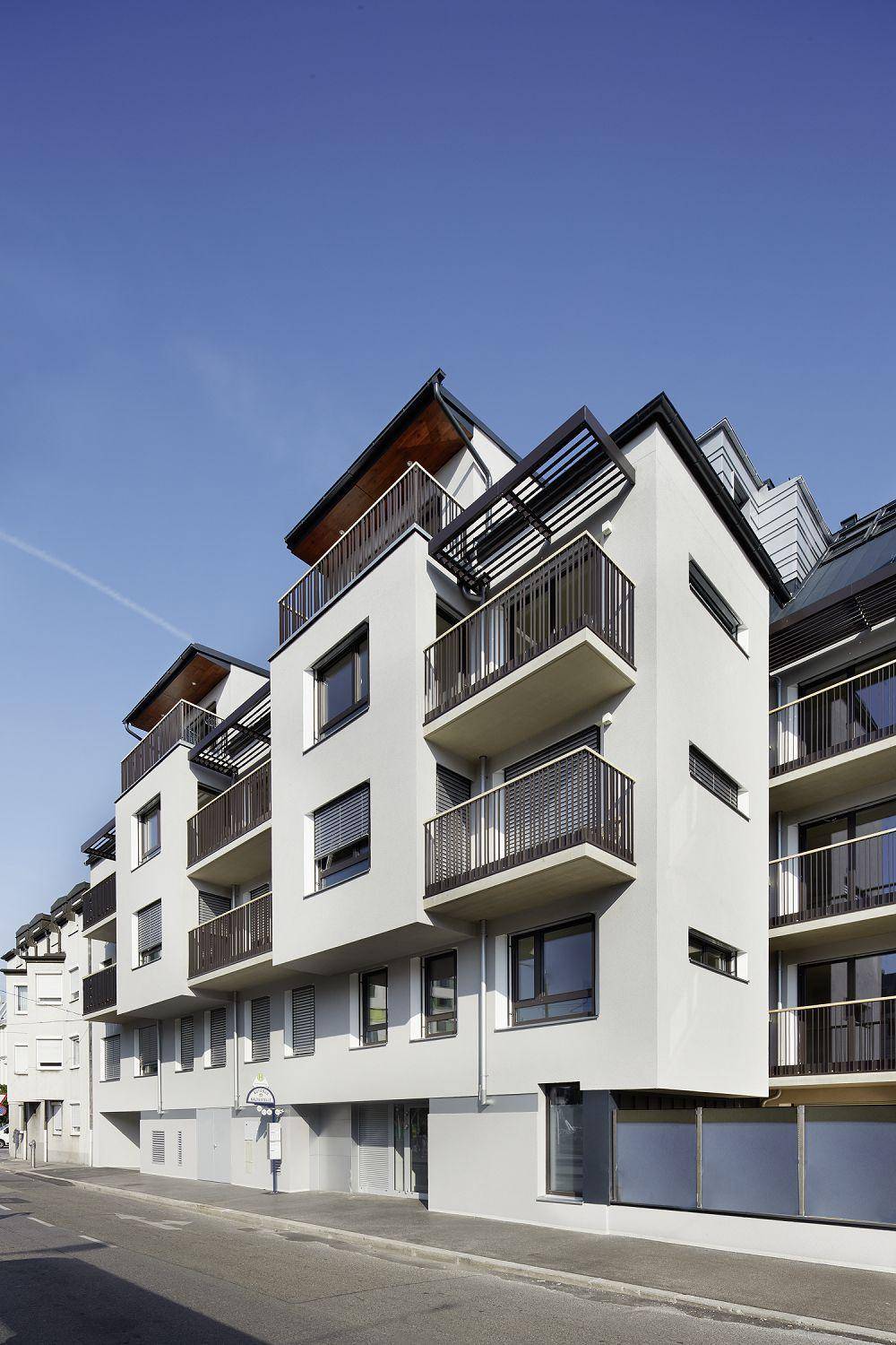 Modernes Mehrfamilienhaus mit mehreren Balkonen, großen Fenstern und einer klaren Architektur an der Straße.