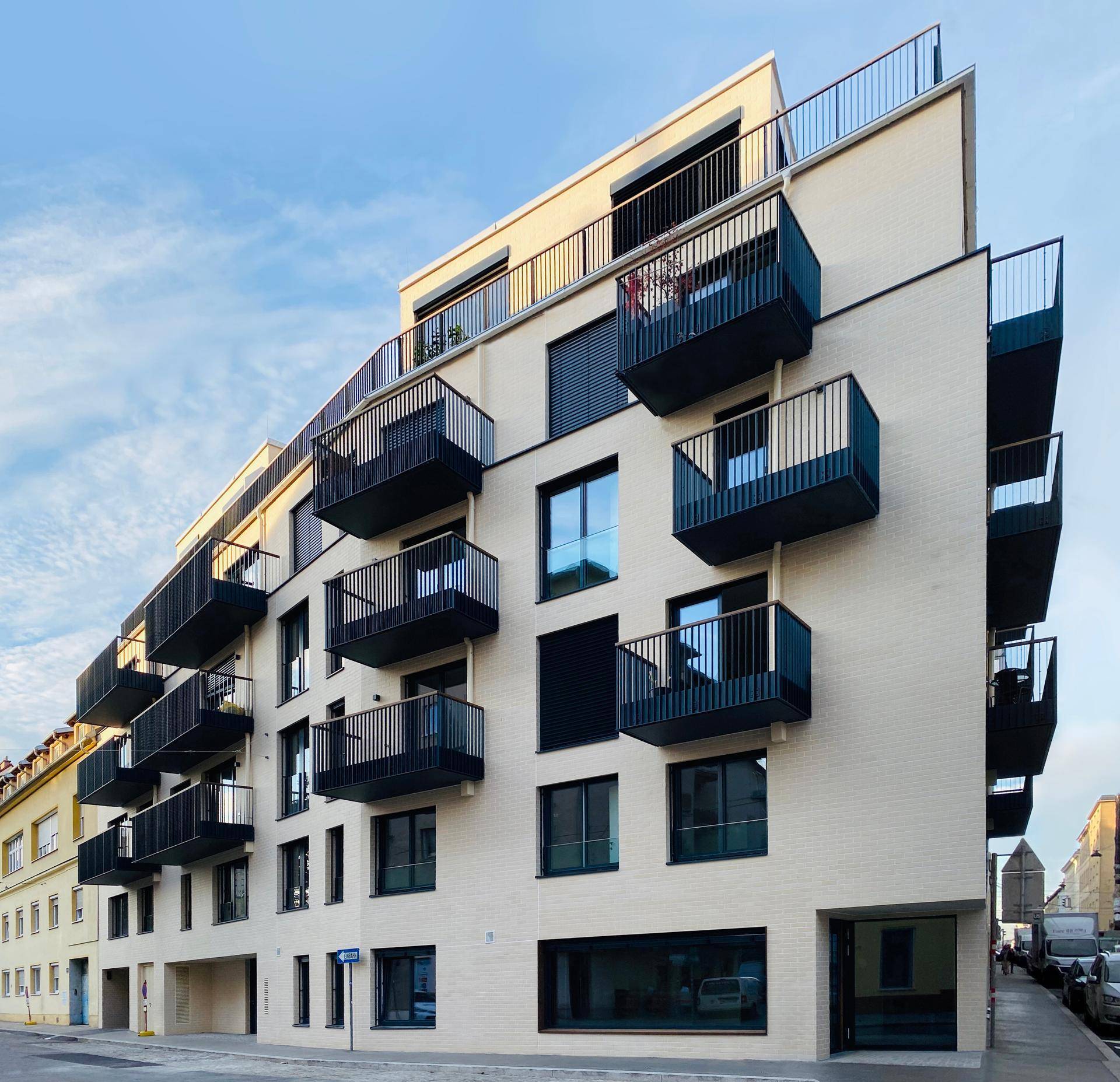Modernes Mehrfamilienhaus mit beiger Fassade, zahlreichen Balkonen und großen Fenstern.