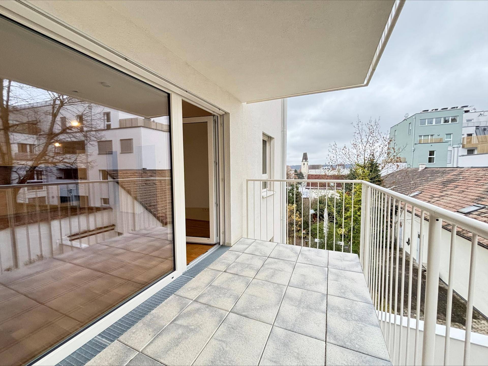 Geräumiger Balkon mit Fliesenboden und Blick auf die umliegenden Gebäude.