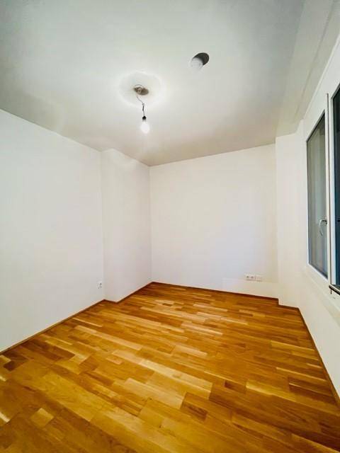 Helles Zimmer mit Parkettboden und einem großen Fenster, bereit zur Einrichtung.