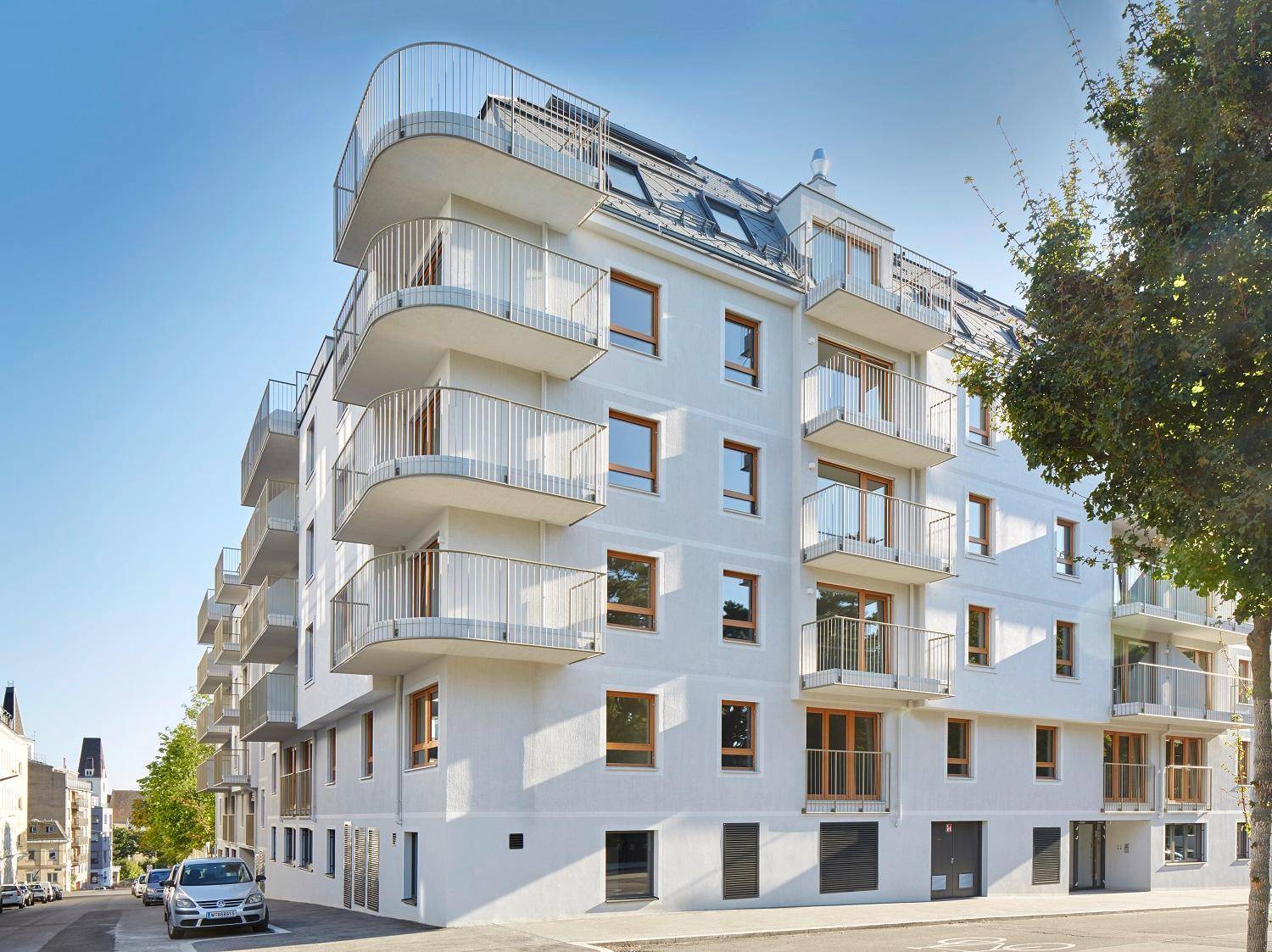 Eckansicht eines modernen Mehrfamilienhauses mit geschwungenen Balkonen und großen Fenstern.