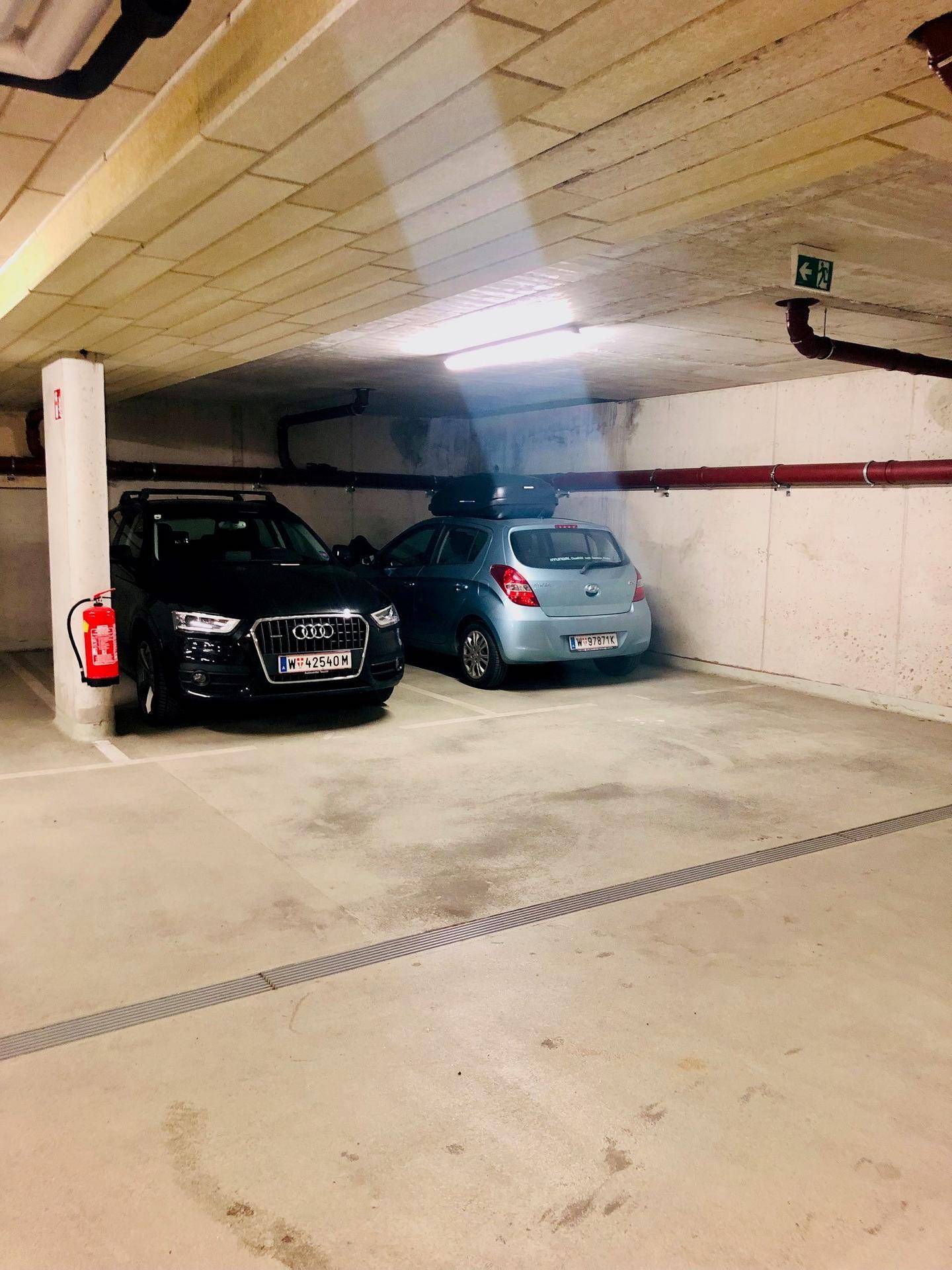 Teilansicht einer Tiefgarage mit zwei geparkten Autos und sichtbaren Installationen an der Decke.