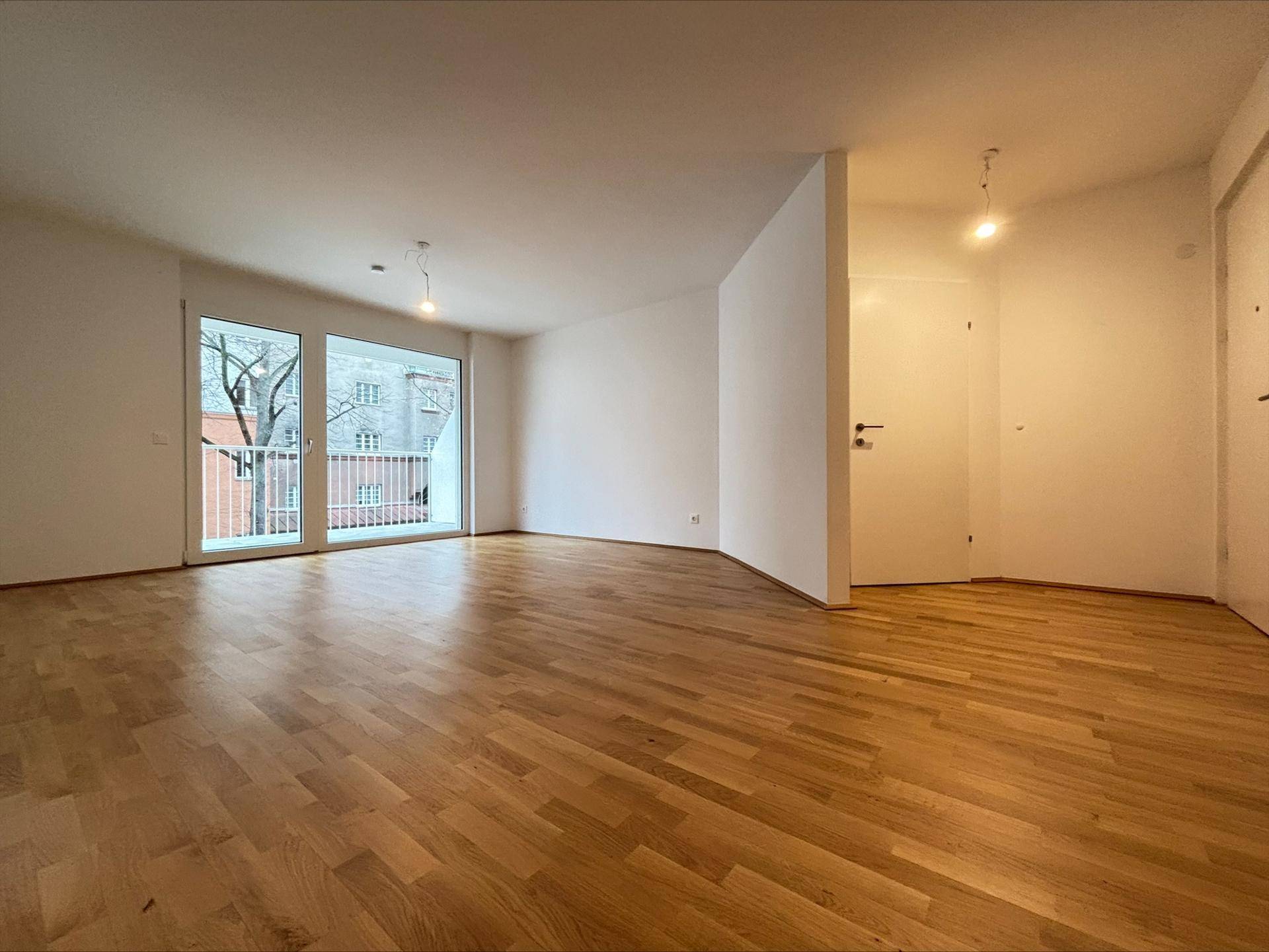 Heller Wohnraum mit Parkettboden, weißen Wänden und Zugang zu einem Balkon.