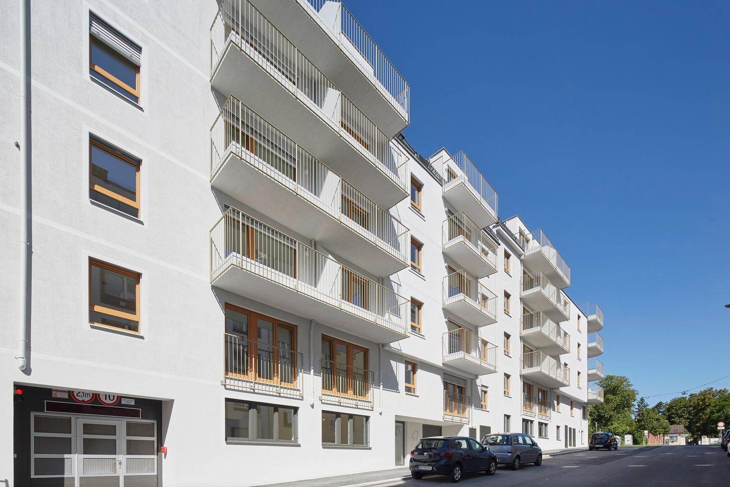 Moderne Wohnanlage mit weißer Fassade und zahlreichen Balkonen unter blauem Himmel.