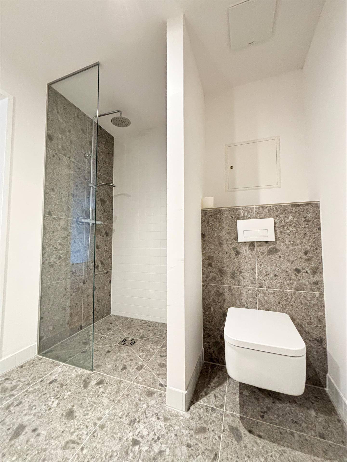 Modernes Badezimmer mit ebenerdiger Dusche, Wand-WC und grauen Fliesen.