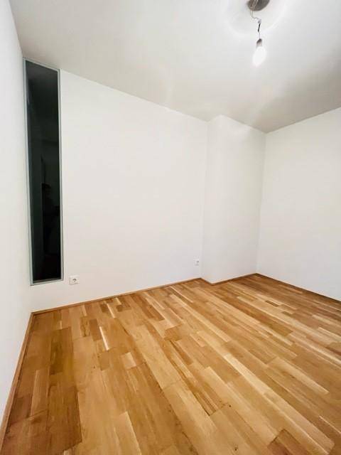 Leeres Zimmer mit Holzparkettboden und einem hohen, schmalen Fenster.