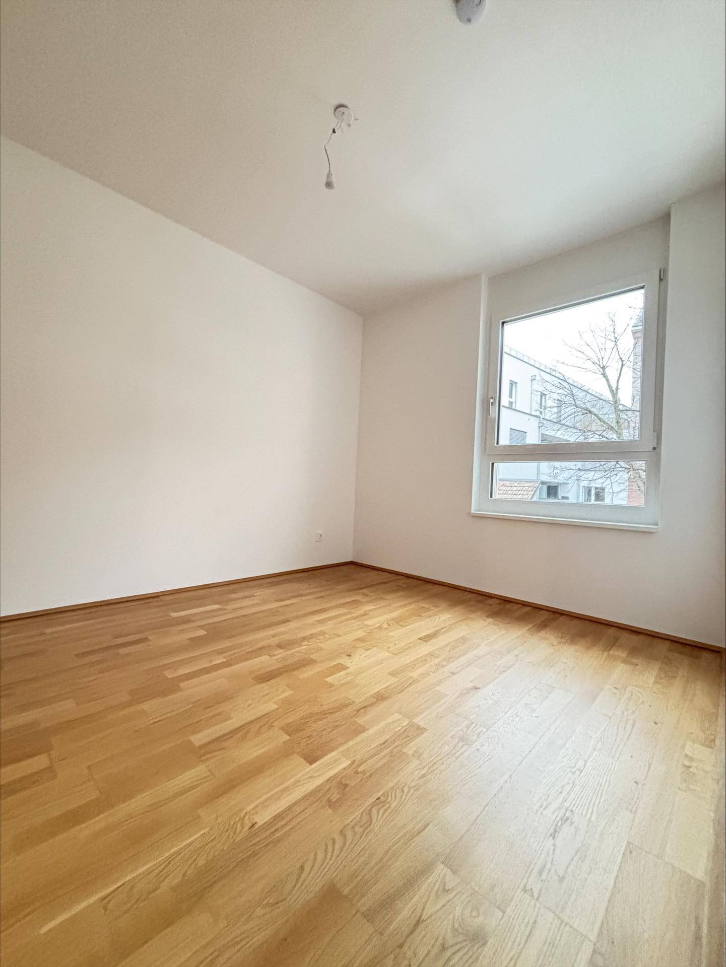 Leeres Zimmer mit Parkettboden und großem Fenster, ideal als Schlafzimmer.