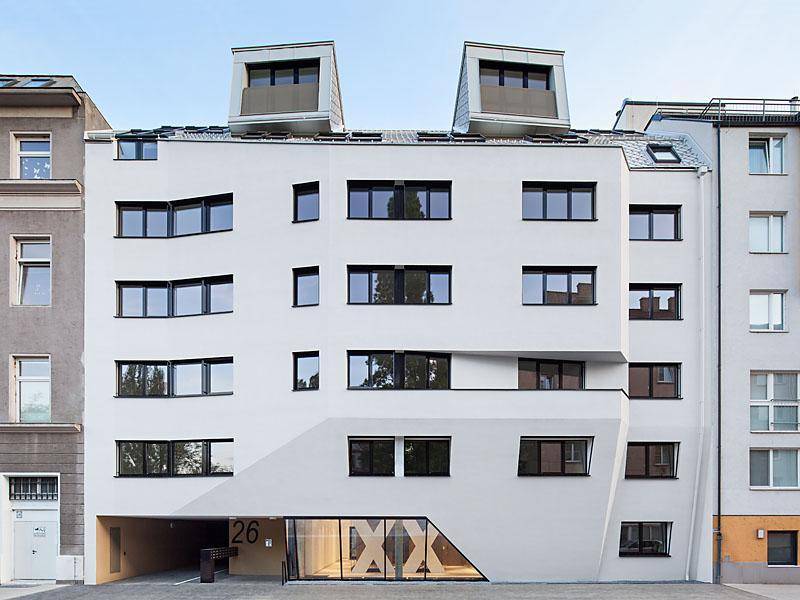 Moderne Wohnhausfassade mit unregelmäßigen Fenstern und einem markanten Eingangsbereich.