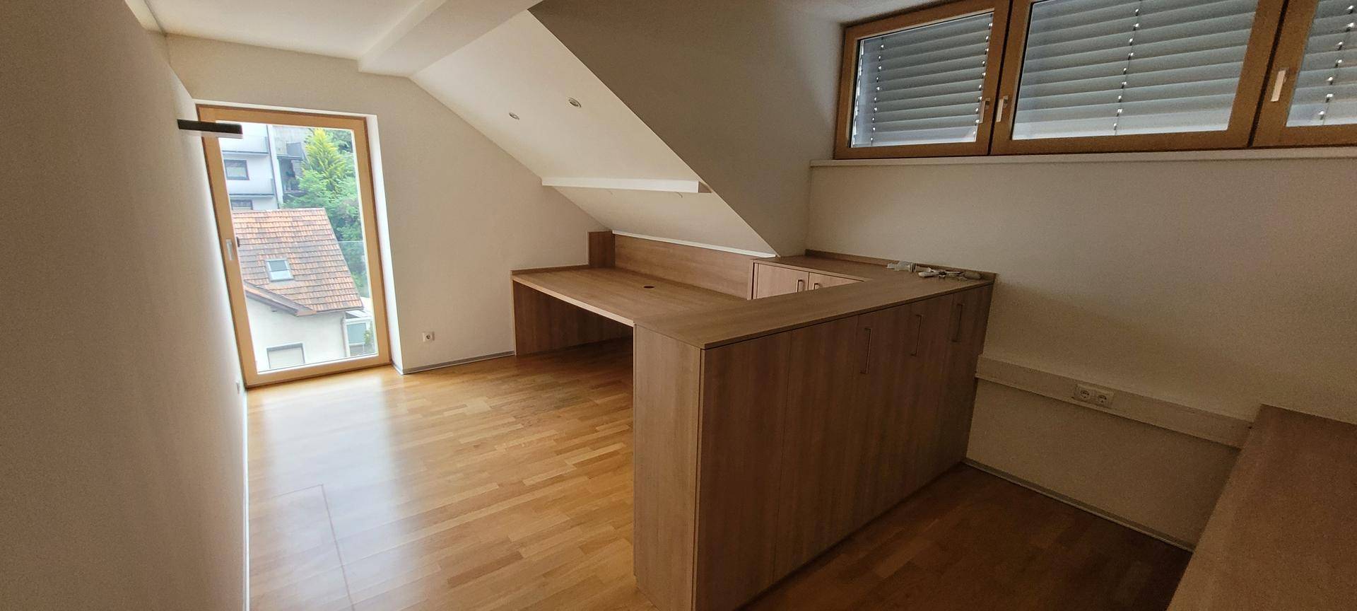 Dachgeschossbüro mit Holzboden, Dachschräge und eingebauten Holzmöbeln.