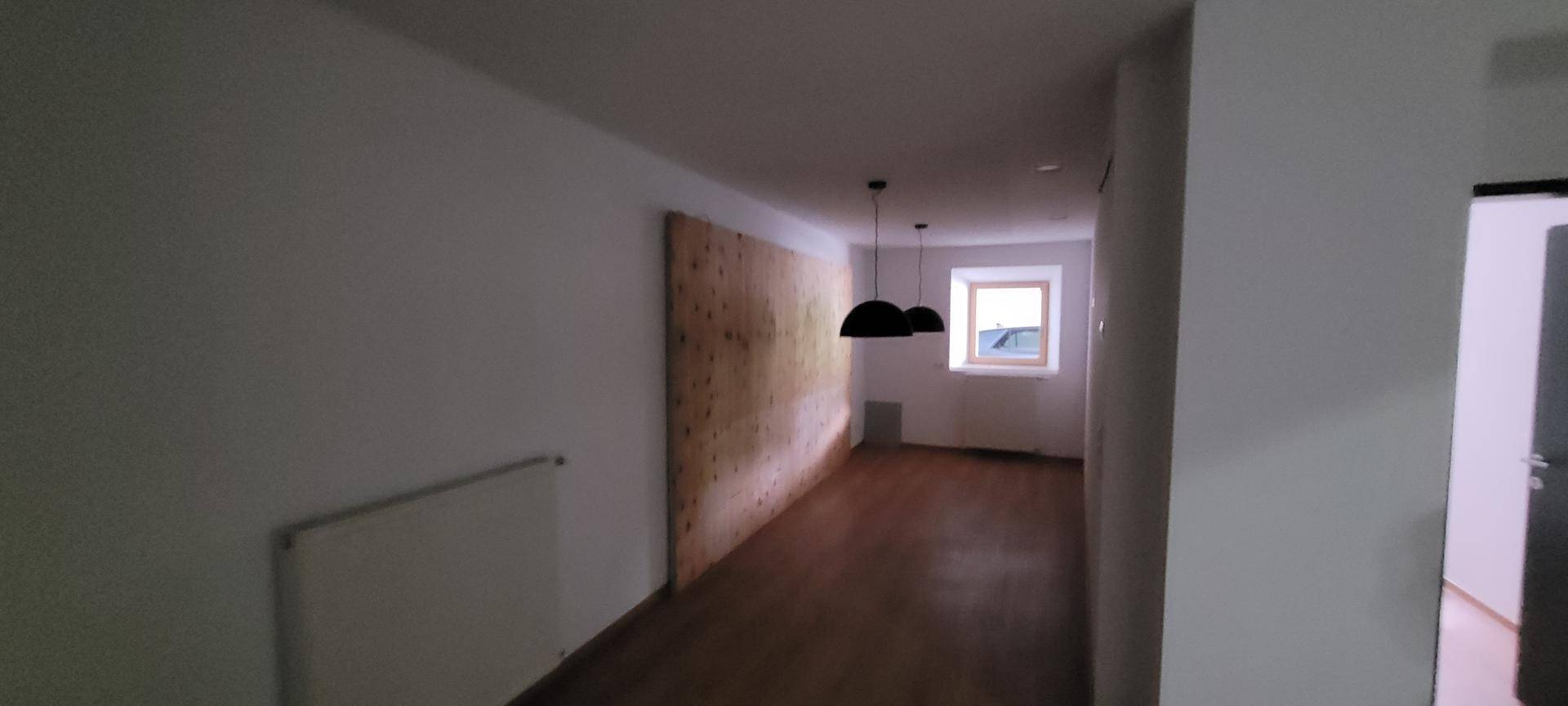 Langer, schmaler Raum mit Holzboden, einer Holzwand und einem Fenster am Ende.