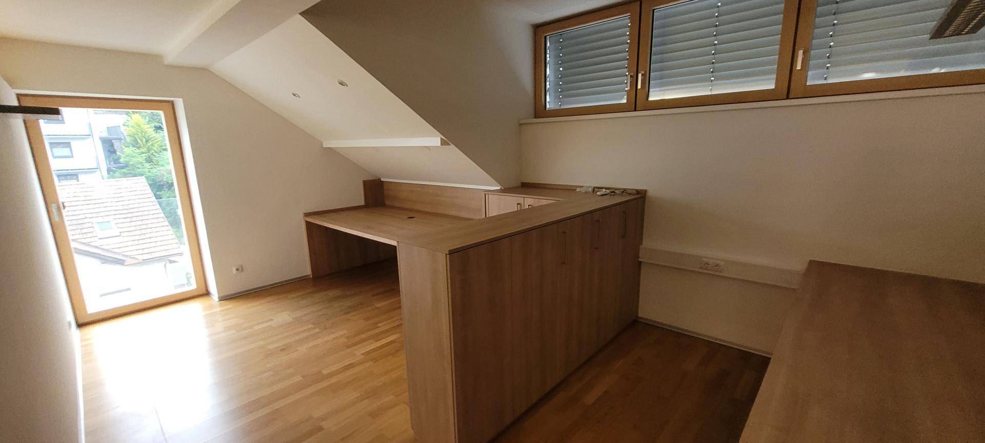 Dachgeschossbüro mit Holzboden, Dachschräge und eingebauten Holzmöbeln.