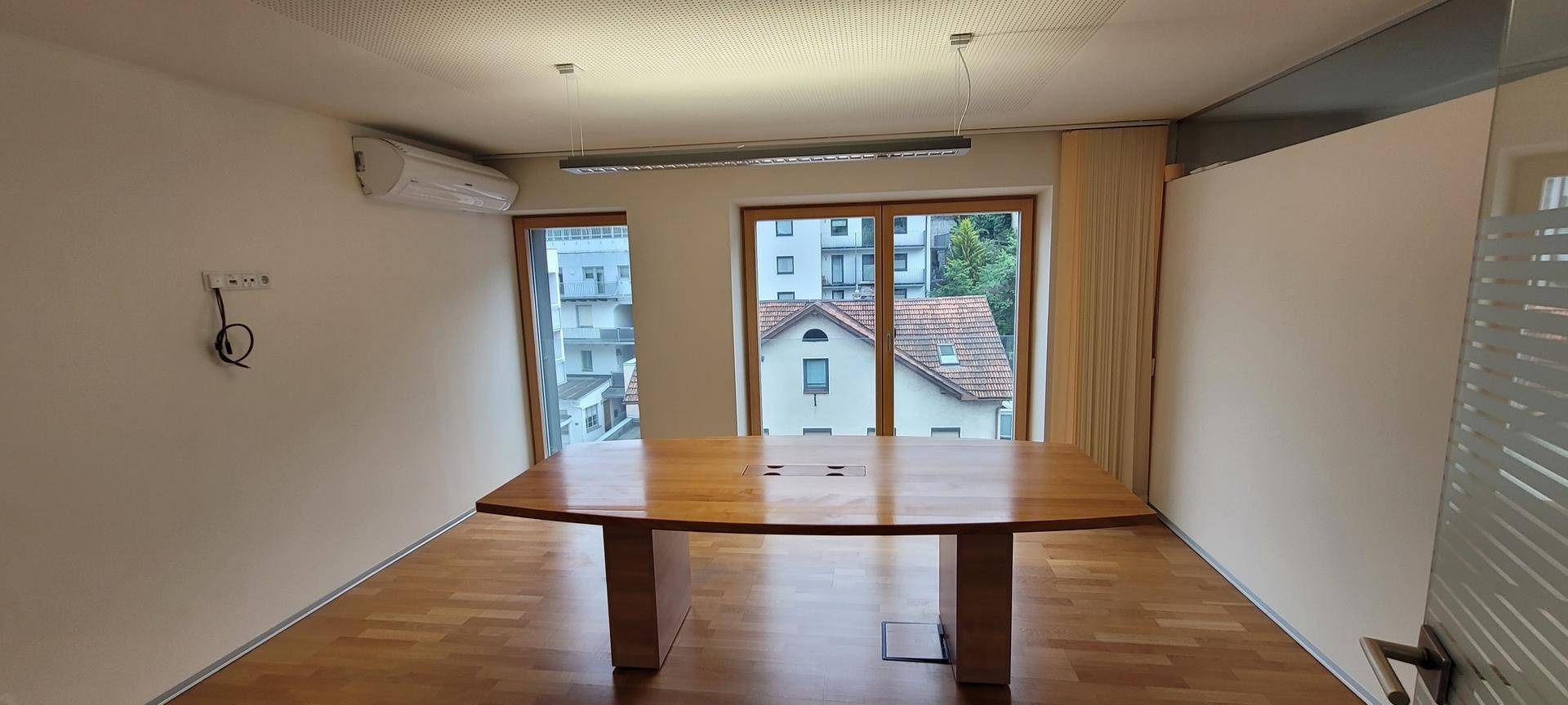 Heller Büroraum mit Holzboden, großem Konferenztisch und Fenstern mit Blick auf die Umgebung.