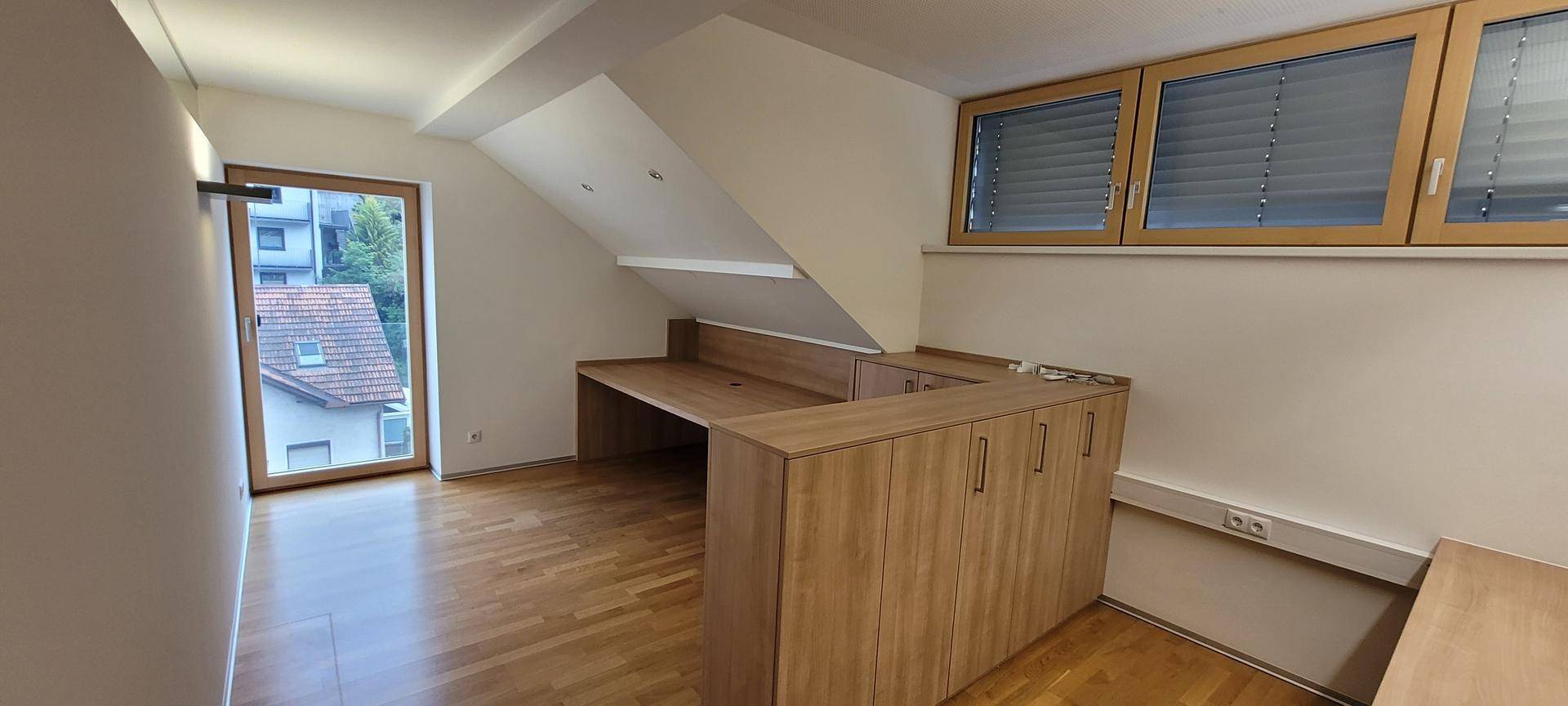 Dachgeschossbüro mit Holzboden, Dachschräge und eingebauten Holzmöbeln.