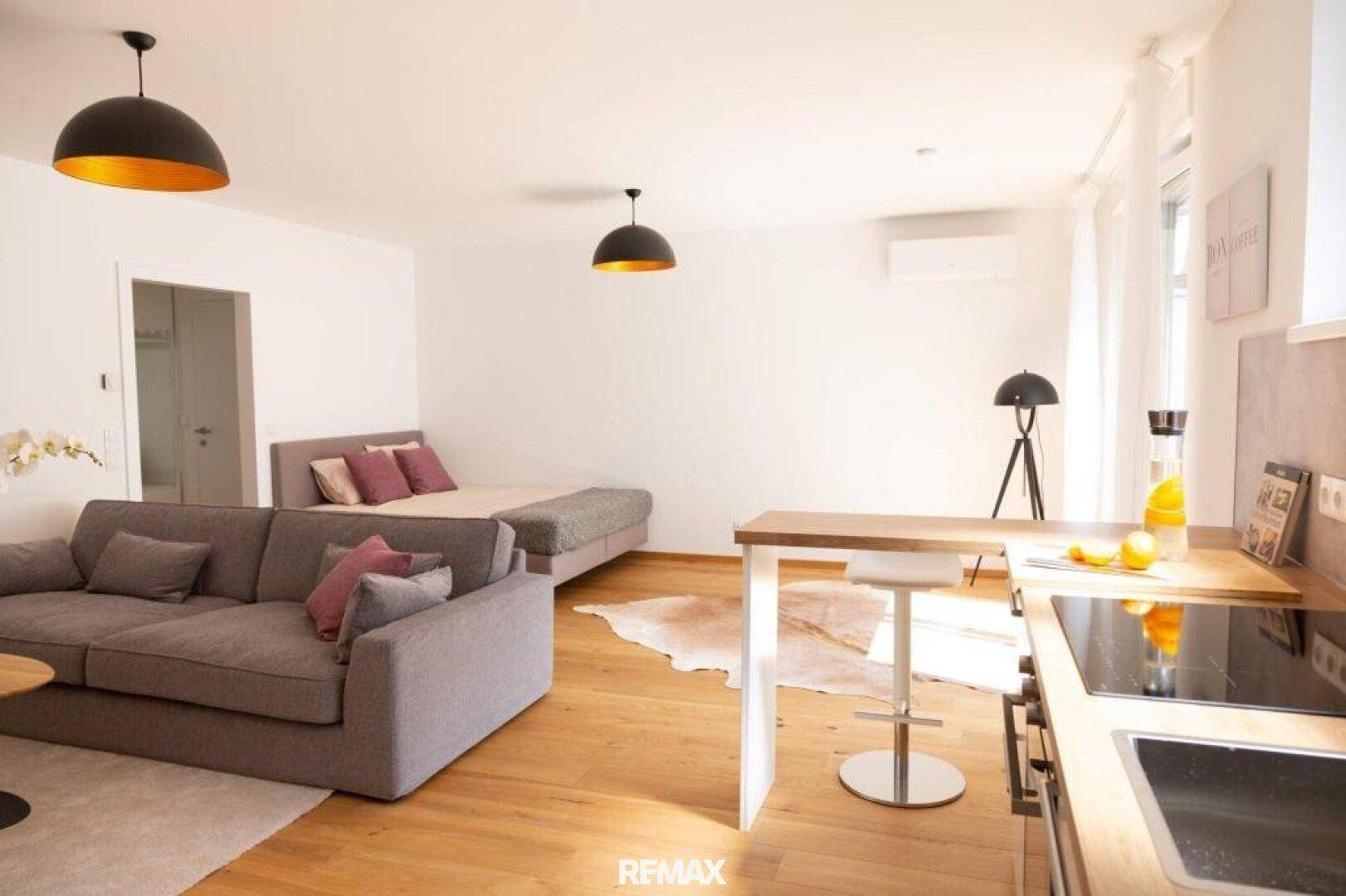 Studio-Apartment mit Schlafbereich, Sofa, offener Küche und modernem Holzboden.