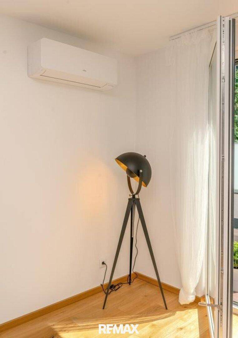 Ecke des Wohnzimmers mit Klimaanlage, Stehlampe und Vorhängen am Terrassenzugang.