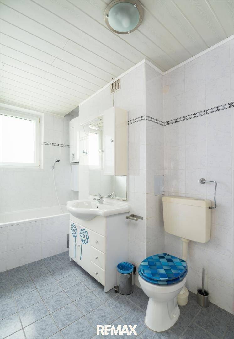 Badezimmer im 80er-Jahre-Stil mit Badewanne, Waschbecken und WC, hell gefliest.