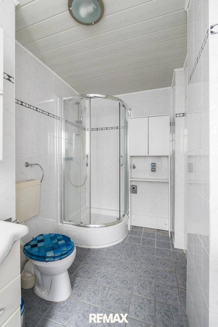 Badezimmer im 80er-Jahre-Stil mit Duschkabine, WC und Waschmaschinenanschluss.