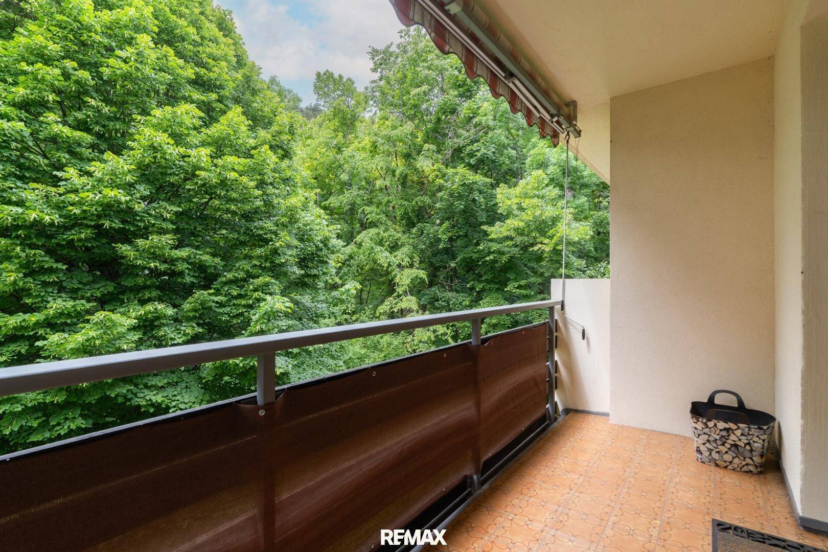Gemütlicher Balkon mit Holzboden und Markise, umgeben von üppigem Grün.