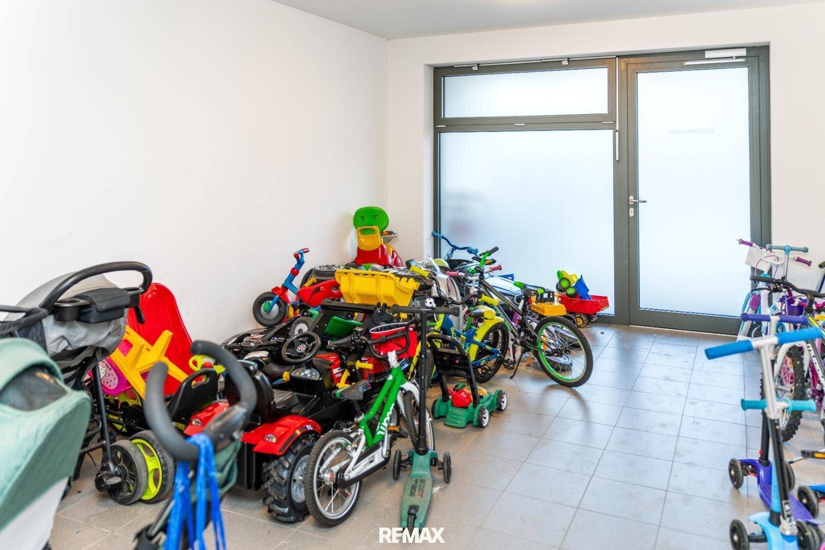 Gemeinschaftlicher Fahrradraum mit vielen Kinderfahrzeugen und Zugangstür.