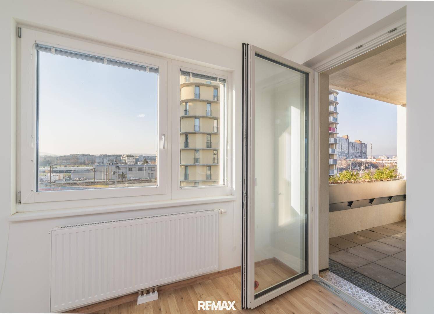 Heller Raum mit großen Fenstern, Holzboden und Zugang zu einem Balkon.
