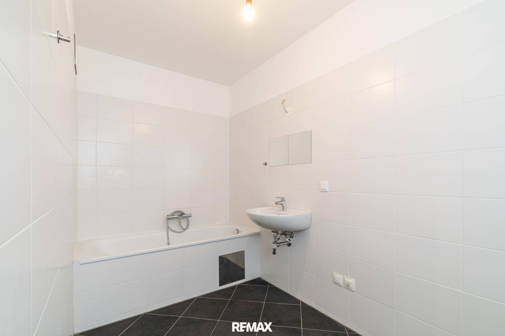 Badezimmer mit weißen Fliesen, Badewanne und Waschbecken.