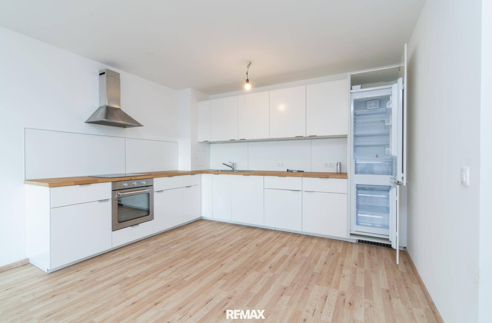 Leere moderne Küche mit weißen Schränken, Holzarbeitsplatte und integriertem Kühlschrank.