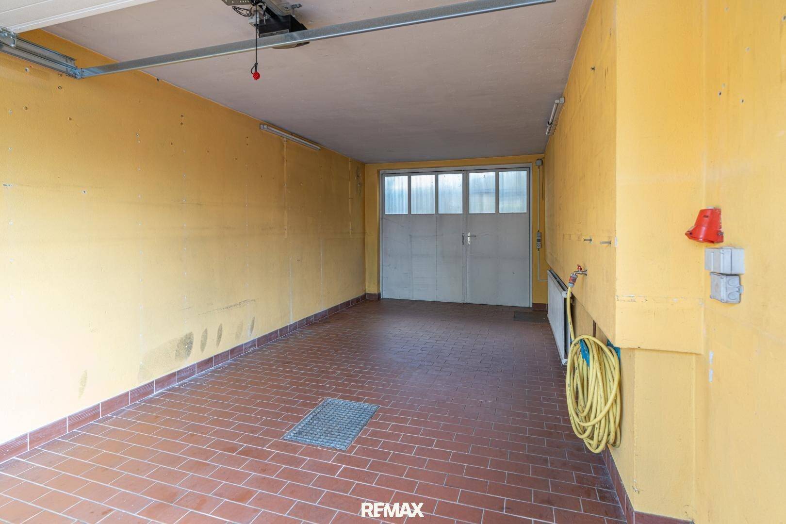 Geräumige Garage mit Fliesenboden und einem großen Garagentor, bereit zur Nutzung.