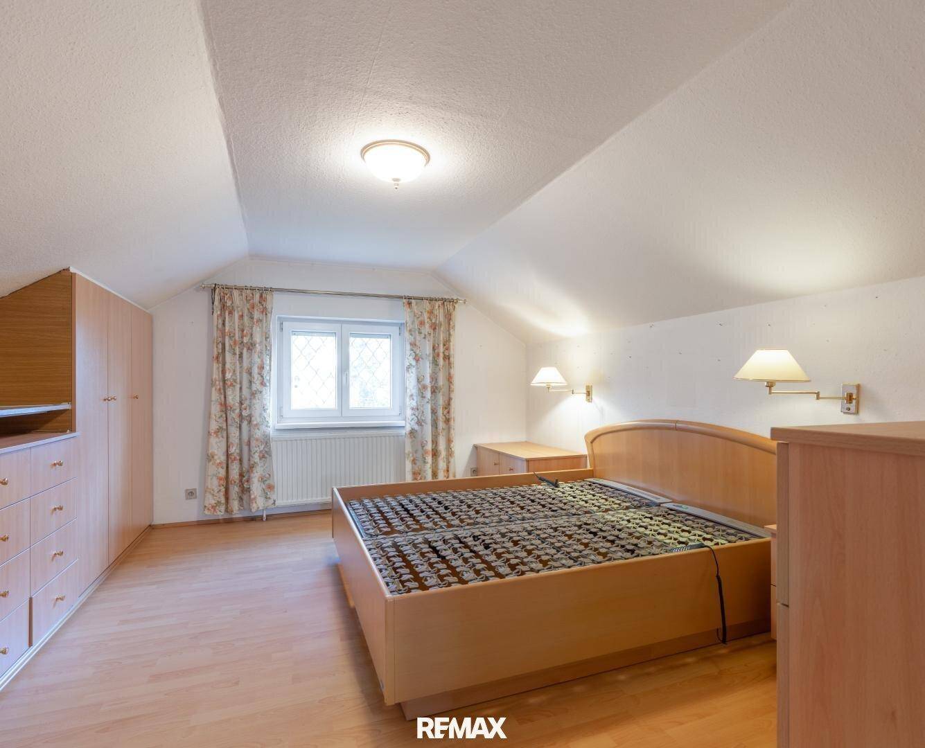 Gemütliches Schlafzimmer mit Holzmöbeln, Dachschräge und einem Fenster für natürliches Licht.