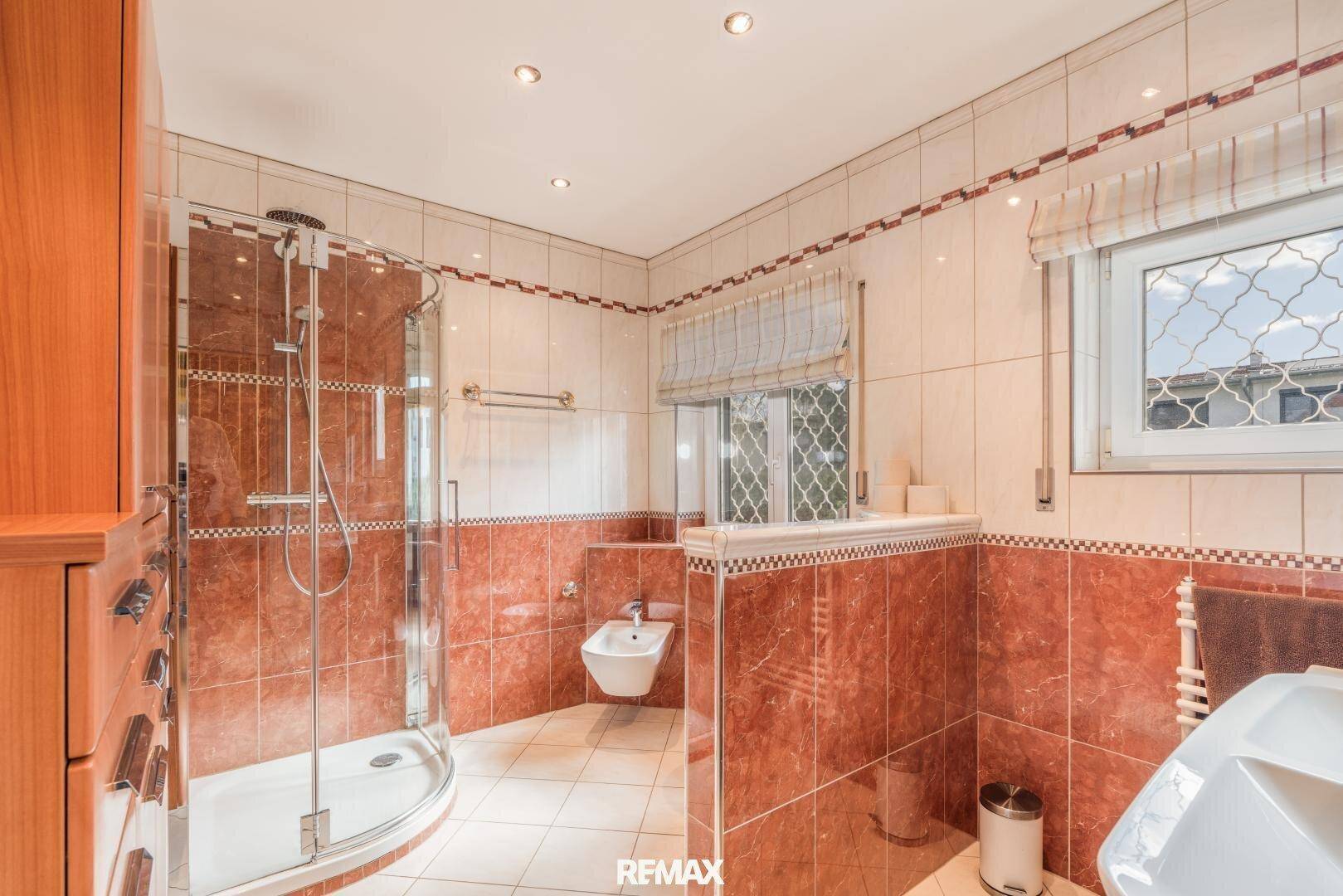 Modernes Badezimmer mit roten Fliesen, Duschkabine, Bidet und einem Fenster für Tageslicht.