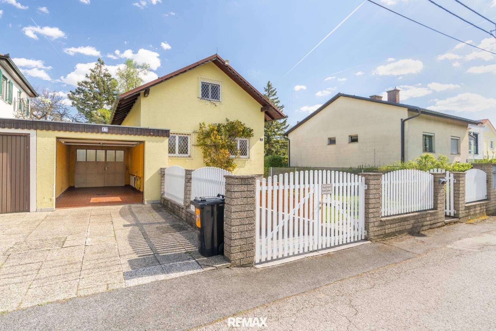Ansicht des Einfamilienhauses von der Straße mit weißem Gartentor, Zufahrt und Garage.