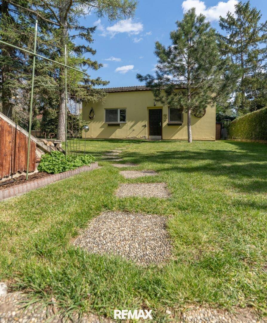 Weitläufiger Garten mit Rasen, Trittsteinen und hohen Bäumen, die Schatten spenden.